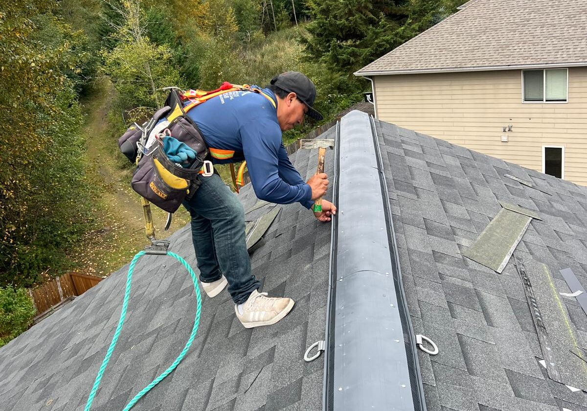 Contractor secures a ridge vent along the roof peak, ensuring proper attic ventilation on a newly shingled home.